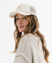 Woman wearing a beige cap with text and a logo on a white background