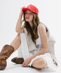 Woman wearing a red cap and brown boots sitting on a white surface