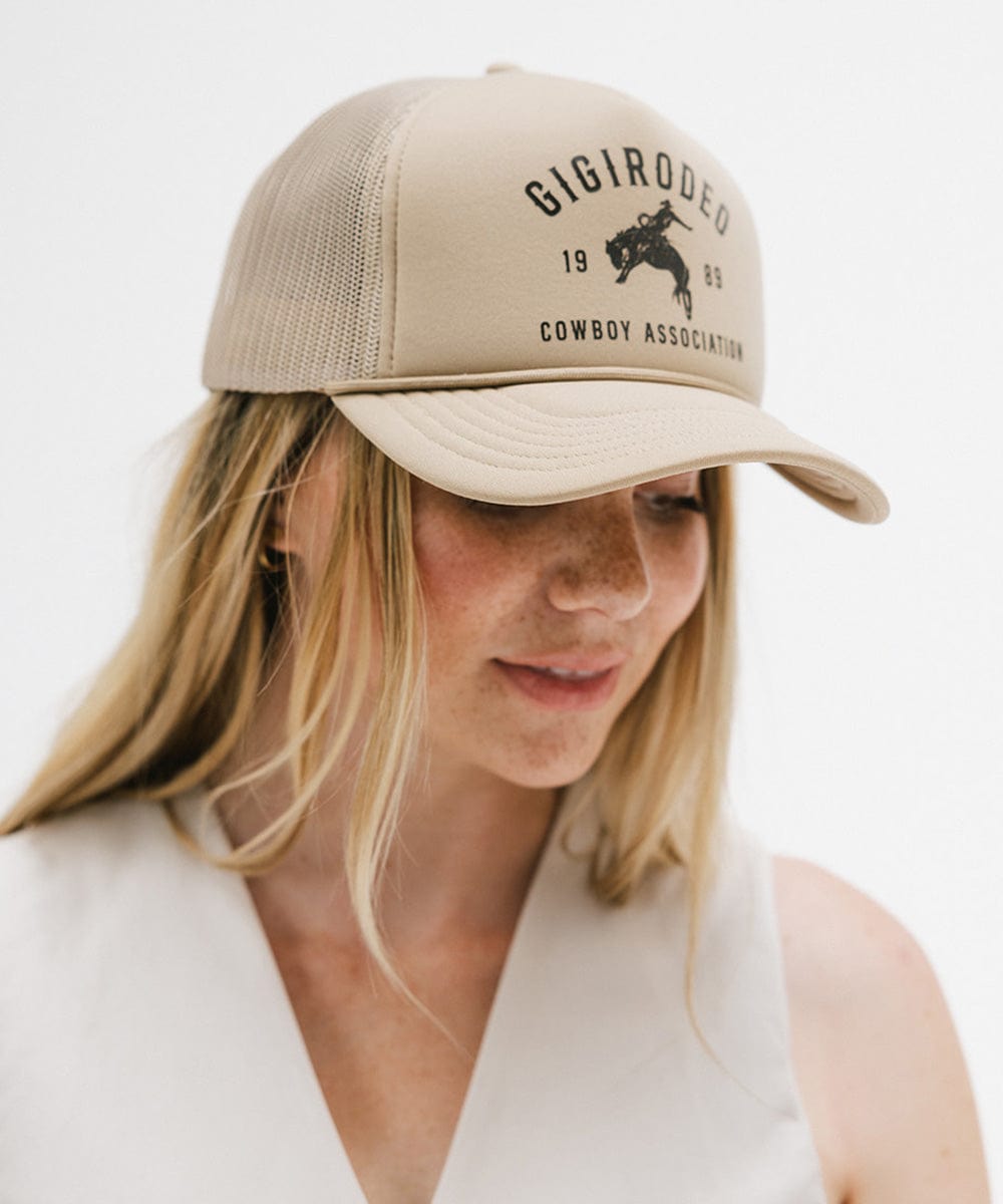Person wearing a beige trucker hat with 'GIGIRODEO' branding on a white background
