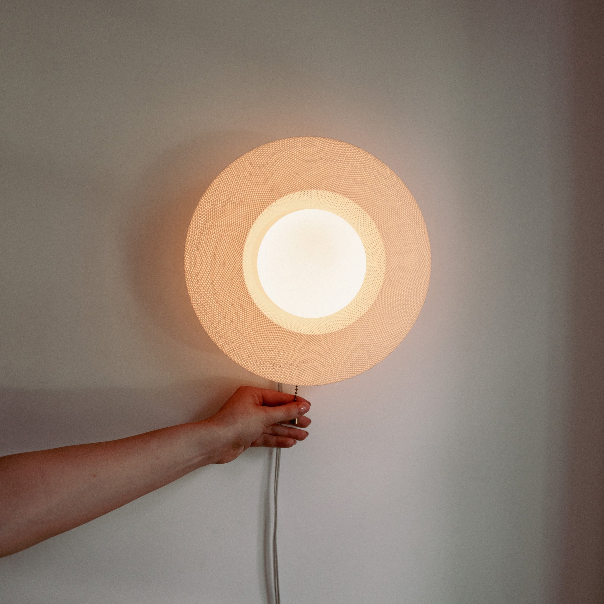 Hand holding a round wall light fixture against a neutral background