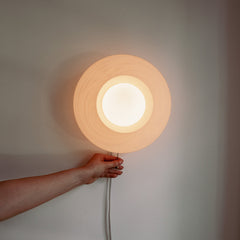 Hand holding a round wall light fixture against a neutral background