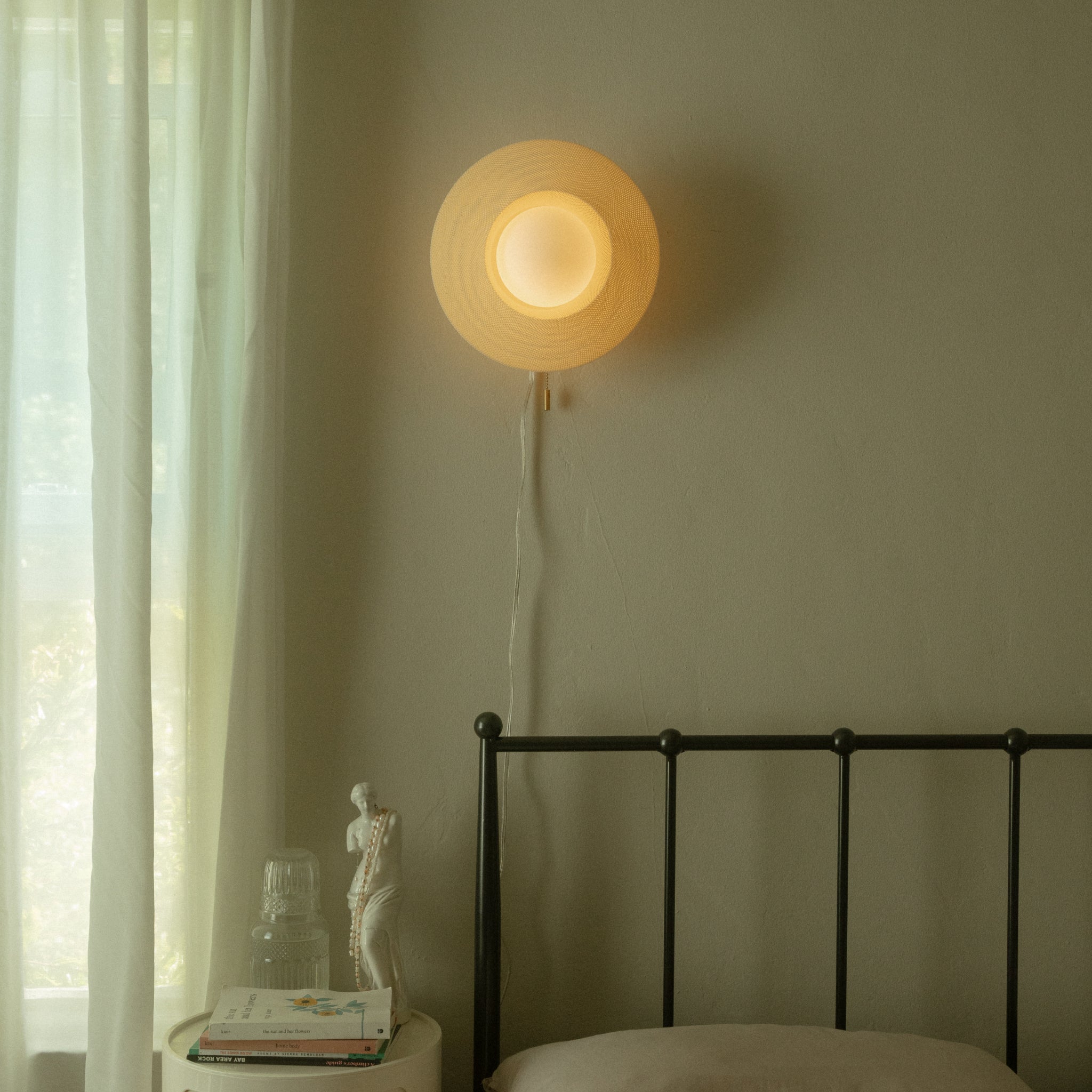 Wall-mounted lamp casting a warm glow in a bedroom setting with a bed and window.