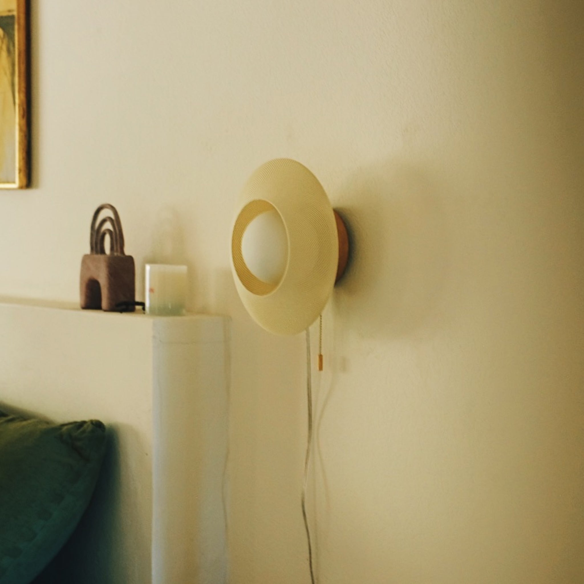 Round wall lamp on a beige wall with a shelf and decorative items in the background.