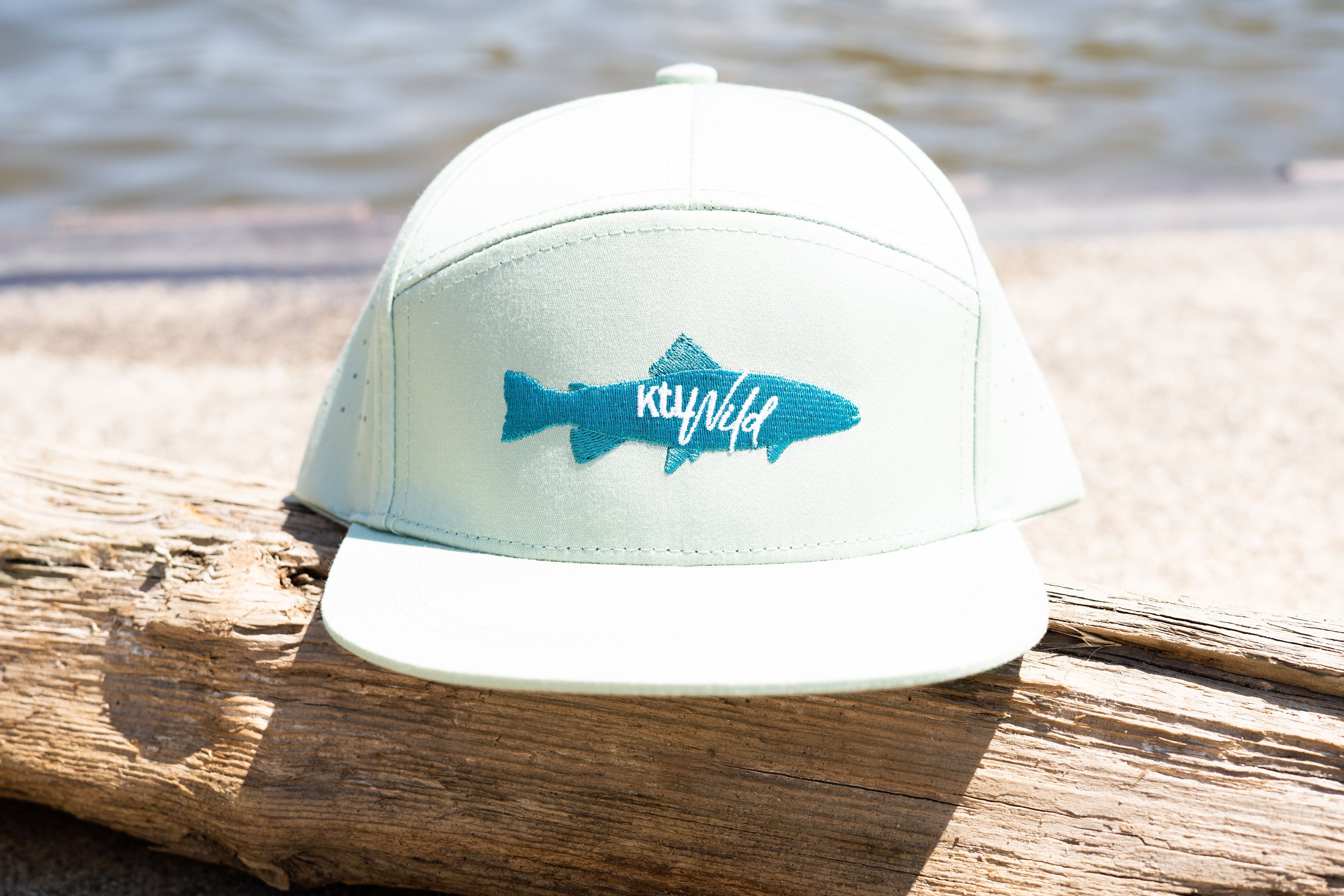White cap with blue fish logo on a wooden log by water