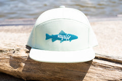 White cap with blue fish logo on a wooden log by water