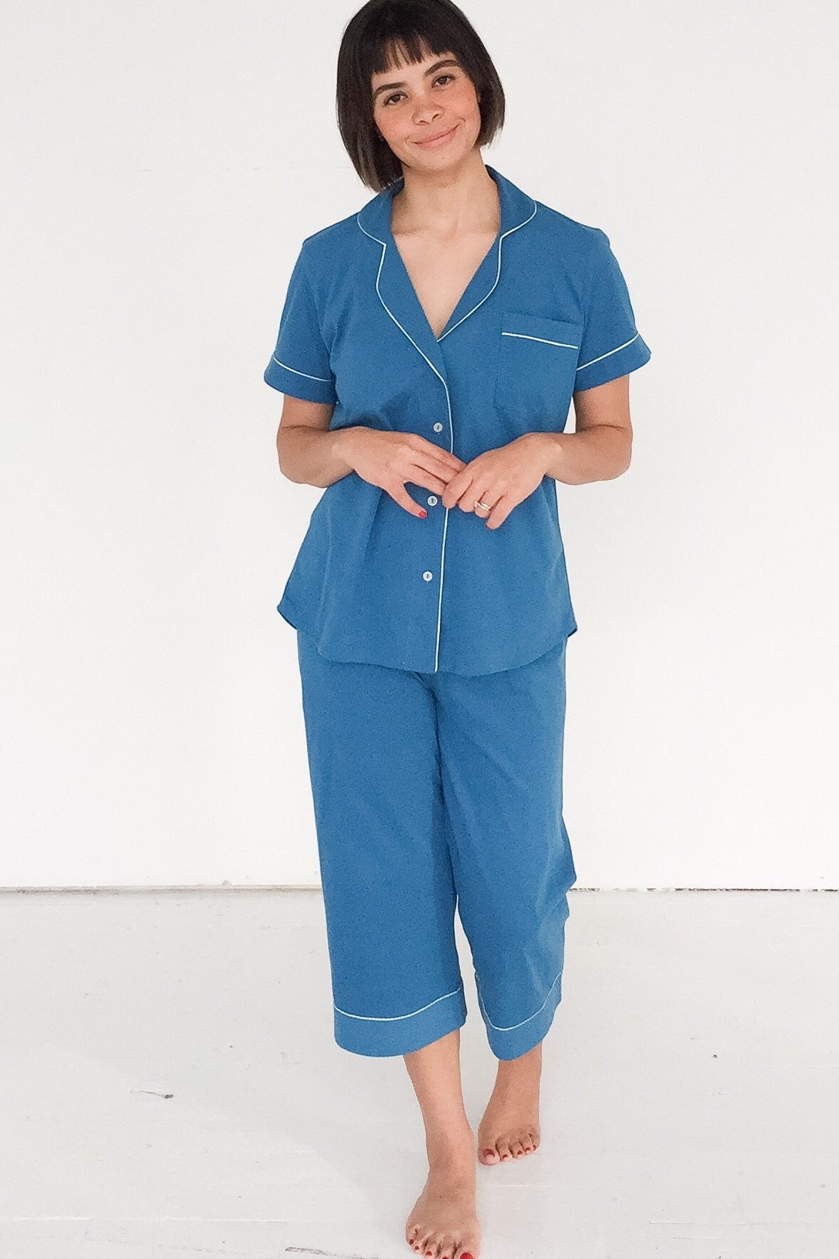 Woman wearing a blue pajama set with white piping on a white background