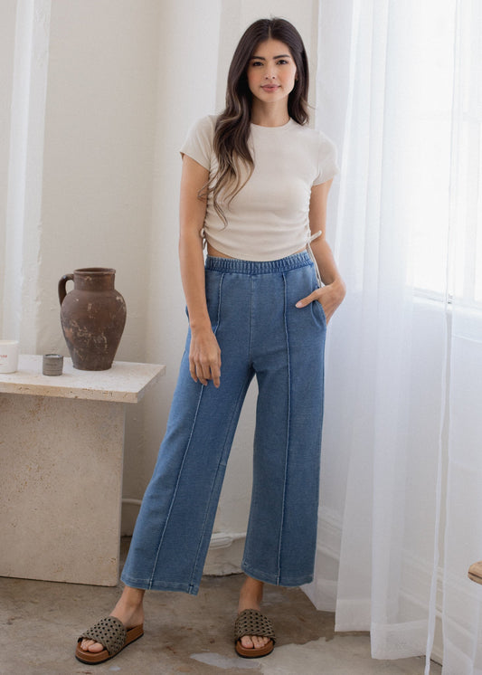 Woman wearing a white t-shirt and blue jeans standing in a room with a vase on a table.