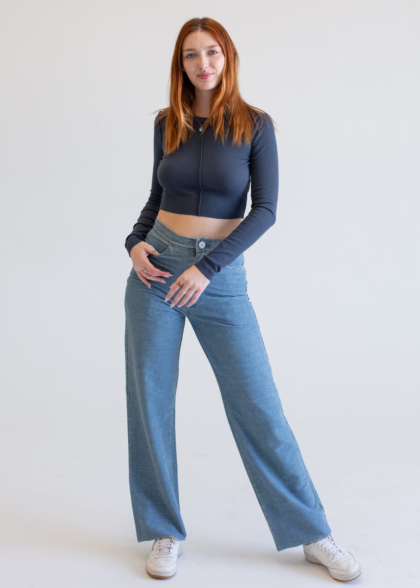 Woman wearing a dark long-sleeve top and blue jeans on a white background