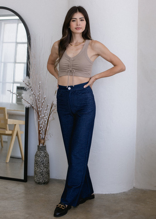Woman wearing a beige top and blue jeans standing indoors.