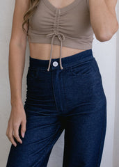 Person wearing a brown crop top and dark blue jeans against a neutral background