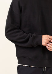 Black hoodie worn by a person on a light beige background