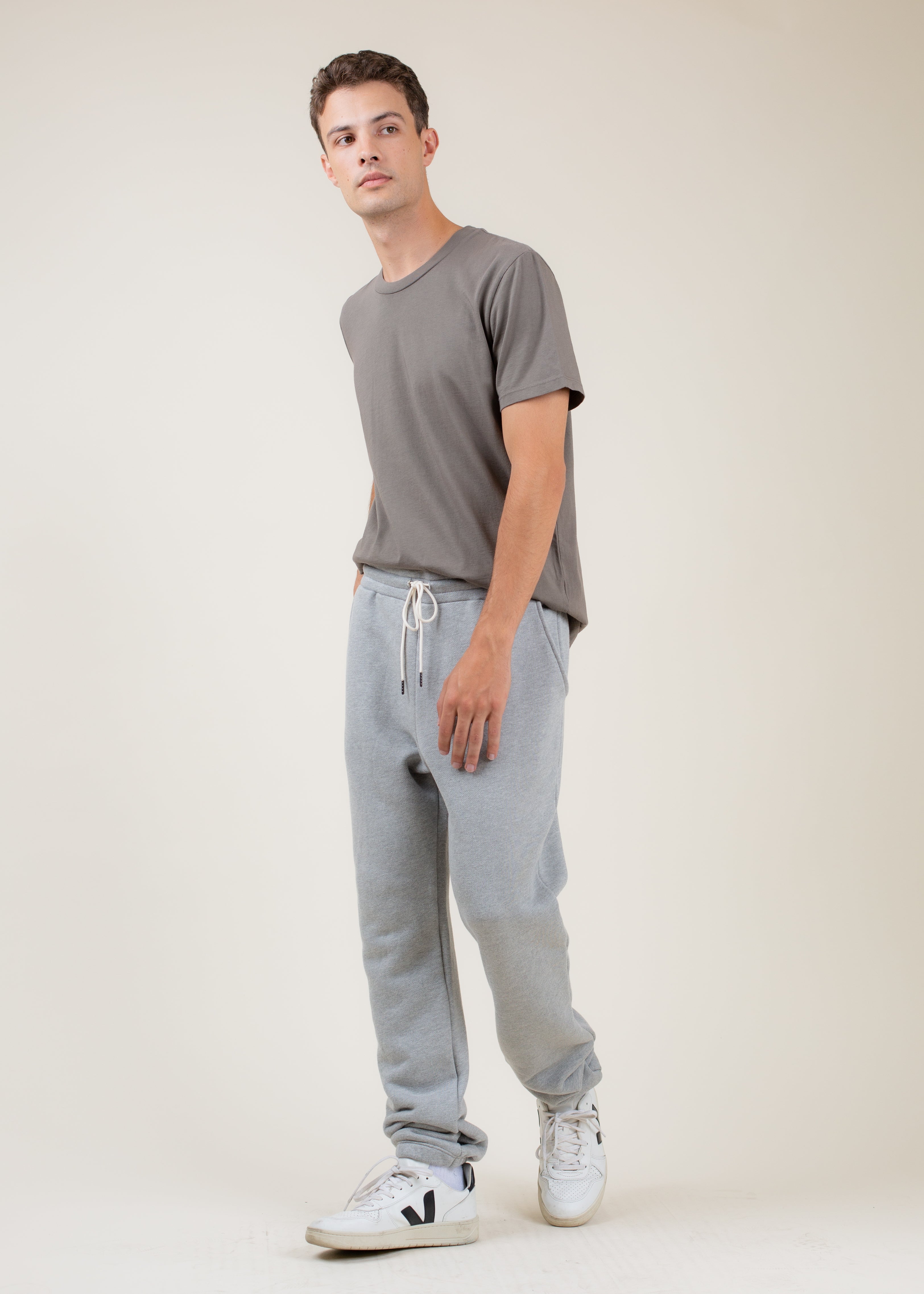 Man wearing a gray t-shirt and light gray sweatpants on a white background