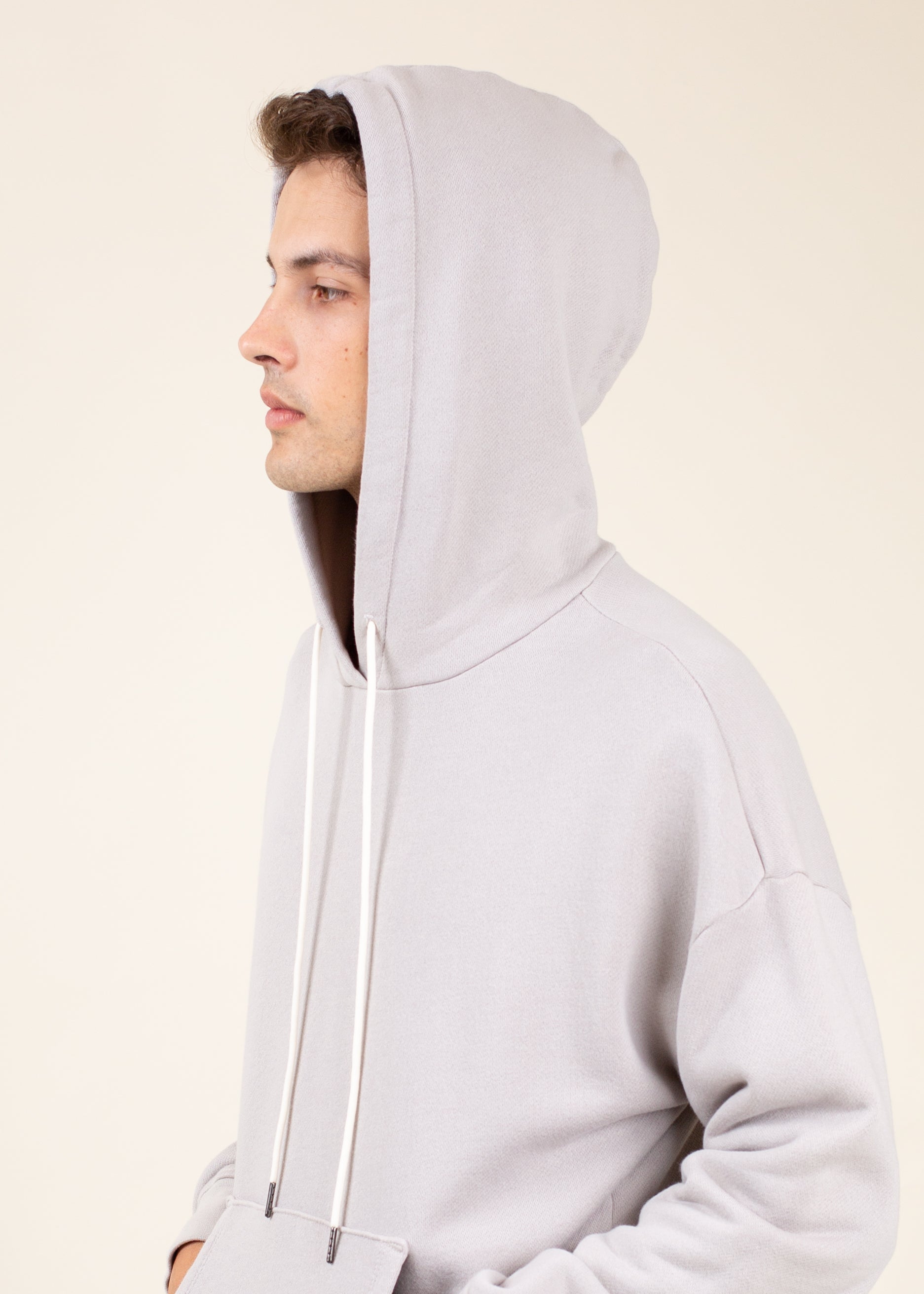 Person wearing a light gray hoodie against a beige background