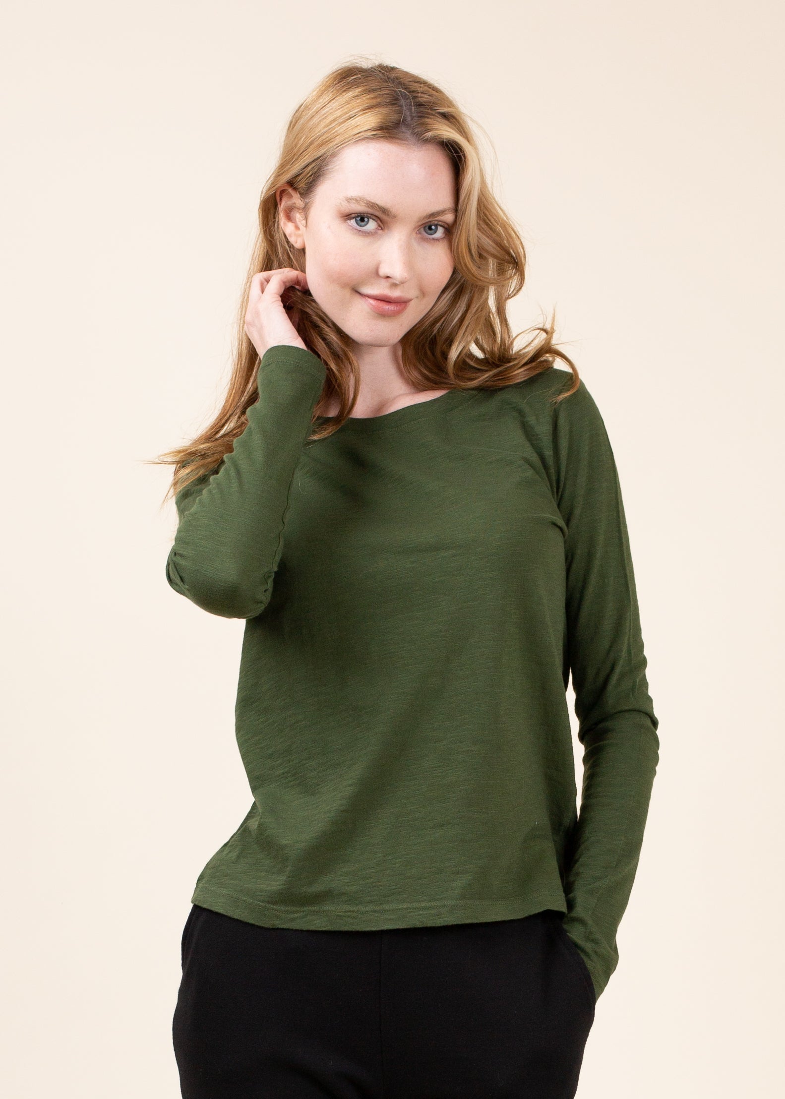 Woman wearing a green long-sleeve top against a beige background