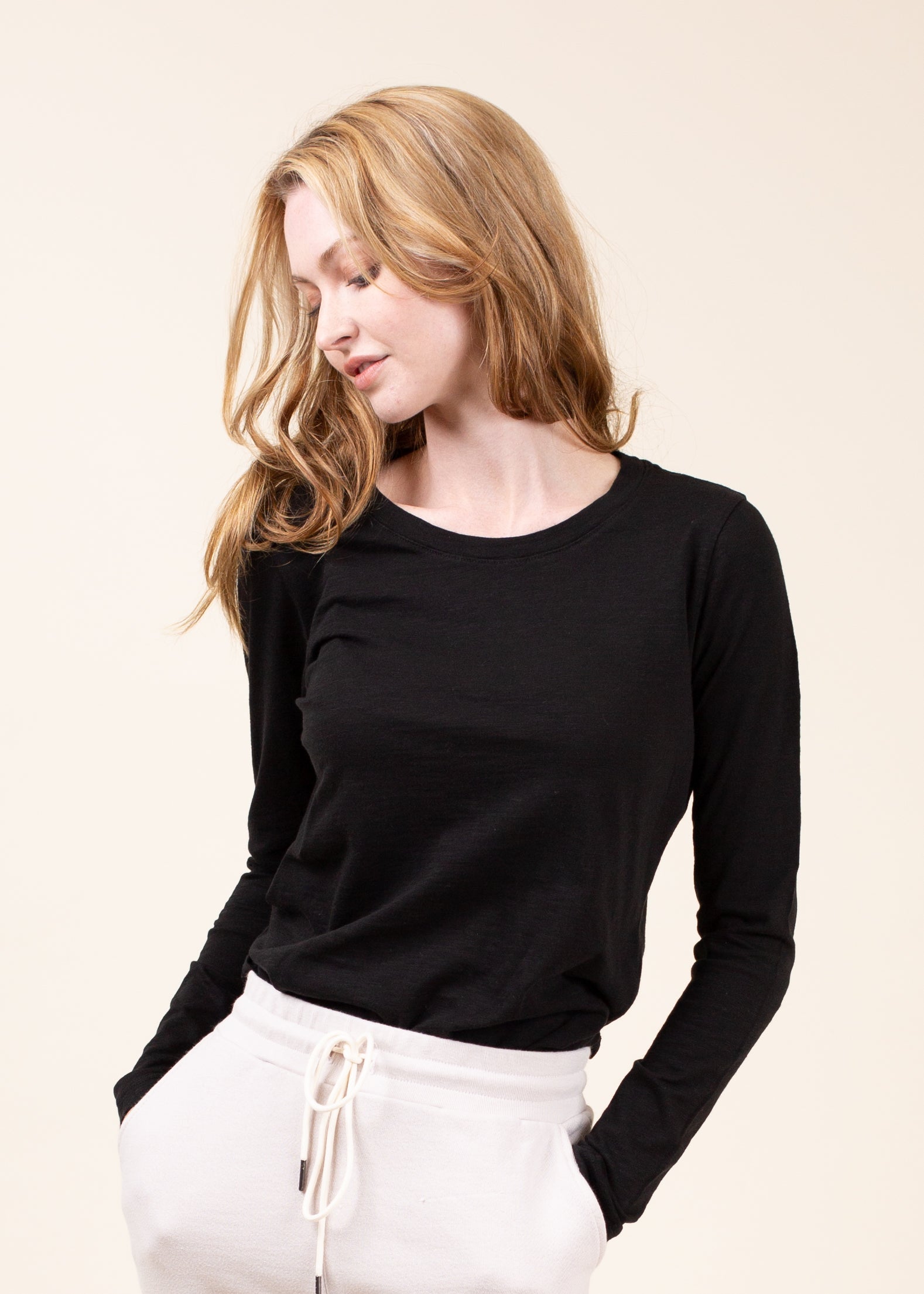 Woman wearing a black long-sleeve top and white pants on a beige background