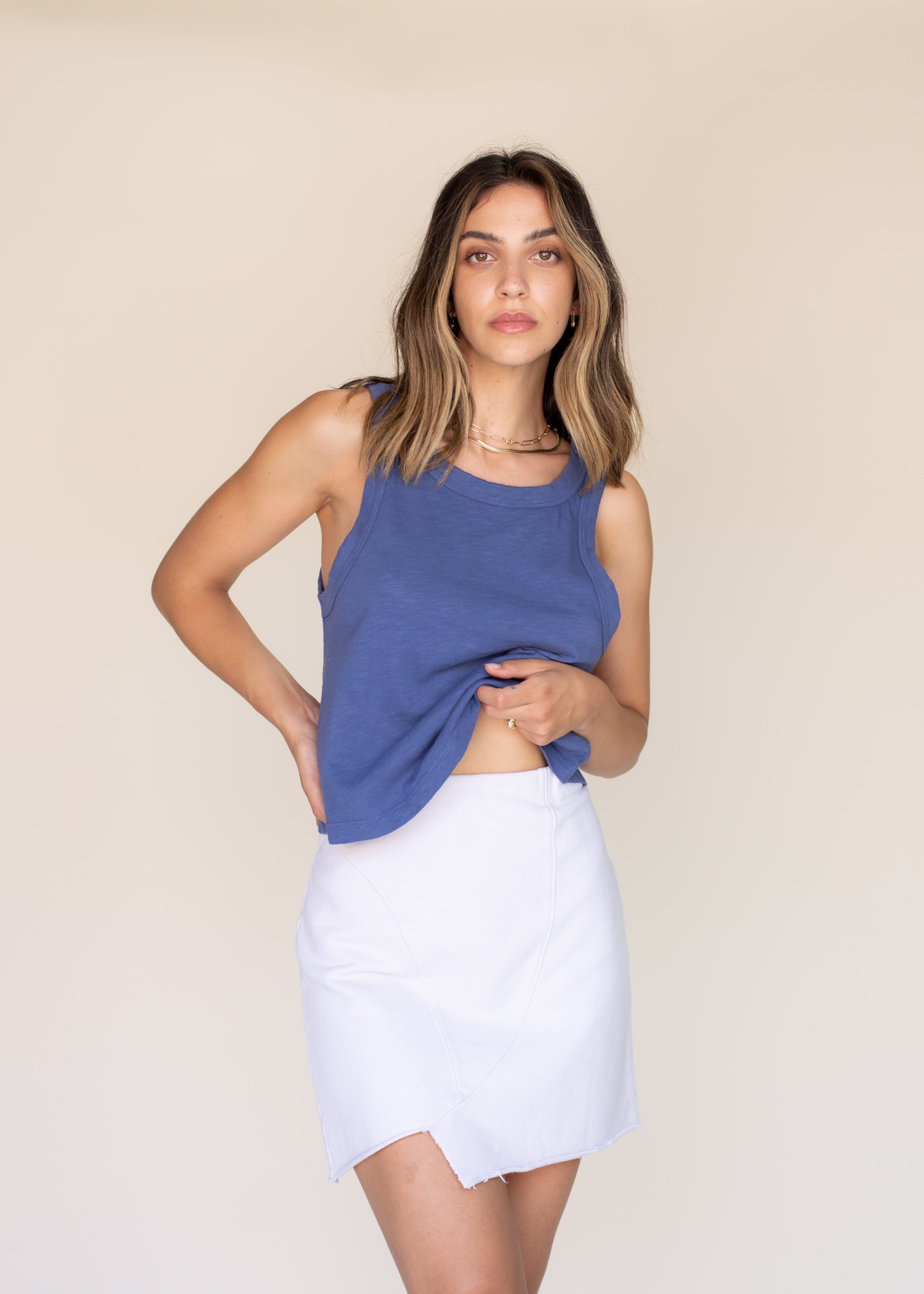 Woman wearing a blue sleeveless top and white skirt against a beige background
