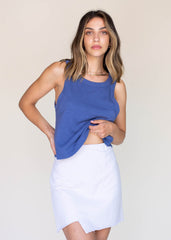 Woman wearing a blue sleeveless top and white skirt against a beige background