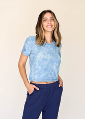 Woman wearing a blue tie-dye crop top and navy pants on a beige background