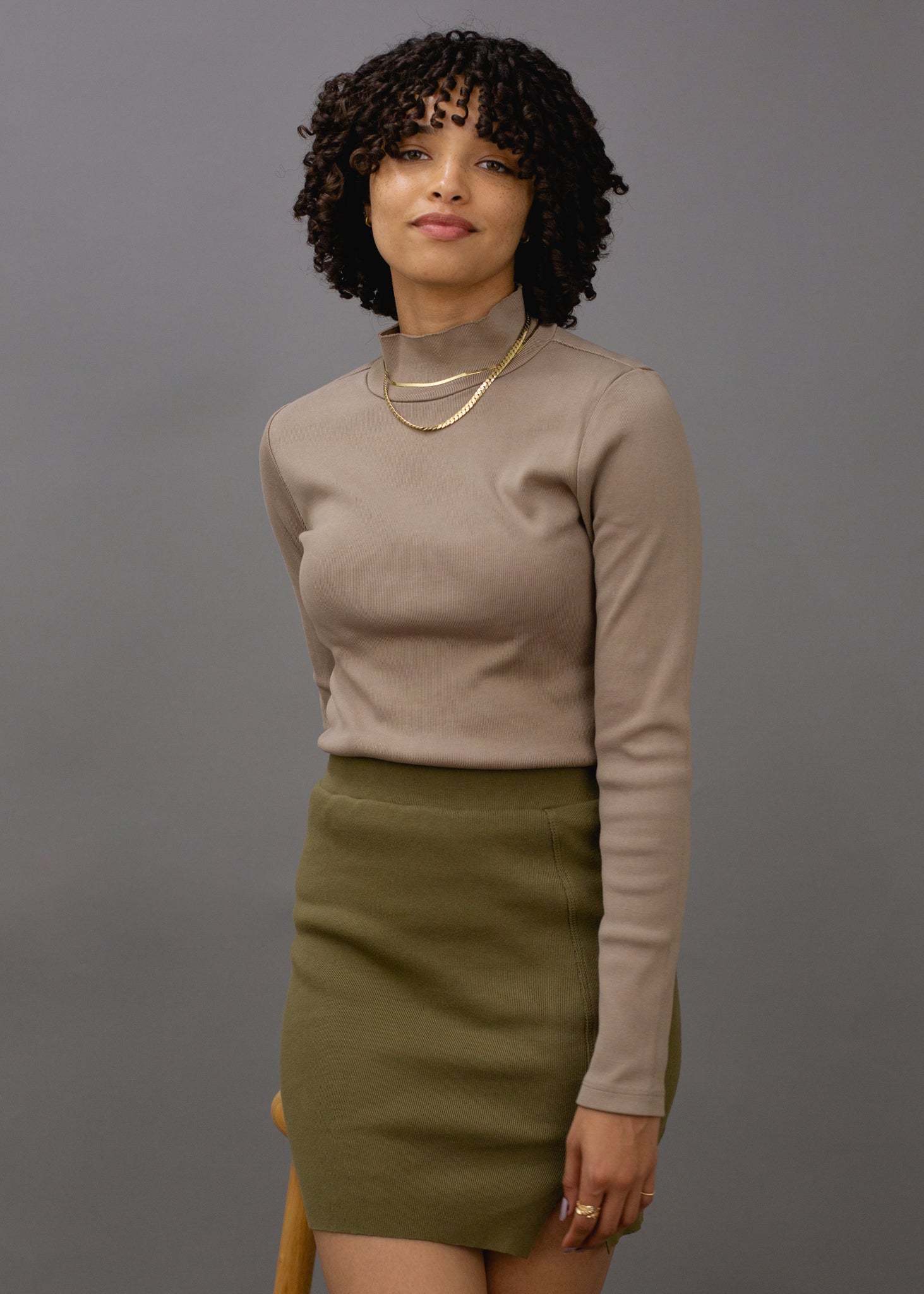 Woman wearing a beige turtleneck and green skirt against a gray background