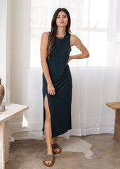 Woman wearing a dark green sleeveless dress with a slit standing in a bright room.