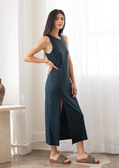 Woman wearing a dark green sleeveless dress with a slit, standing indoors.