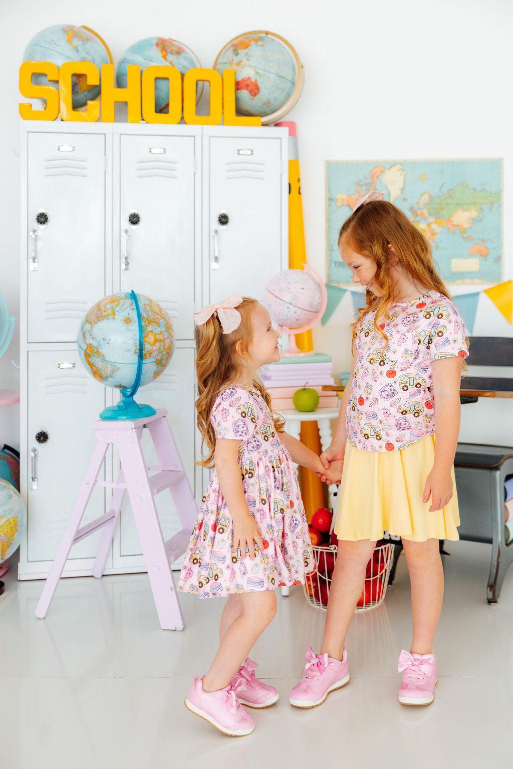 Two young girls standing in a classroom setting with educational decor.