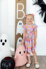Child in a floral dress standing next to Halloween decorations including ghosts and a pink plush toy.