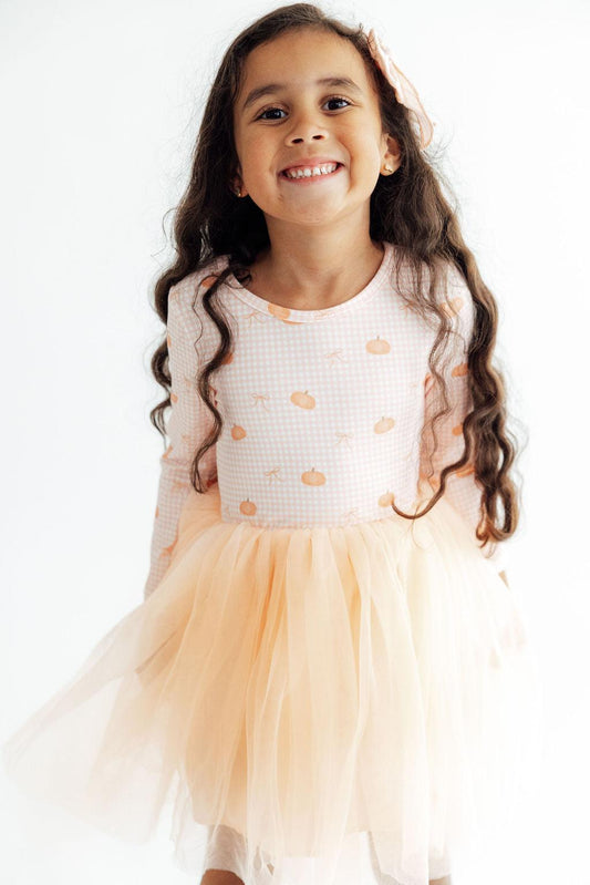 Young girl wearing a white top with orange patterns and a peach-colored tutu skirt on a white background