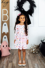 Young girl in a floral dress standing in front of Halloween decorations.