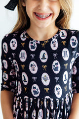 Child wearing a dress with a pattern of cats, houses, and bows on a navy background.