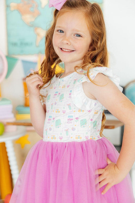Young girl in a dress with a floral top and pink skirt, standing in a colorful room.