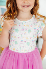 Young girl wearing a white top with colorful patterns and a pink skirt.