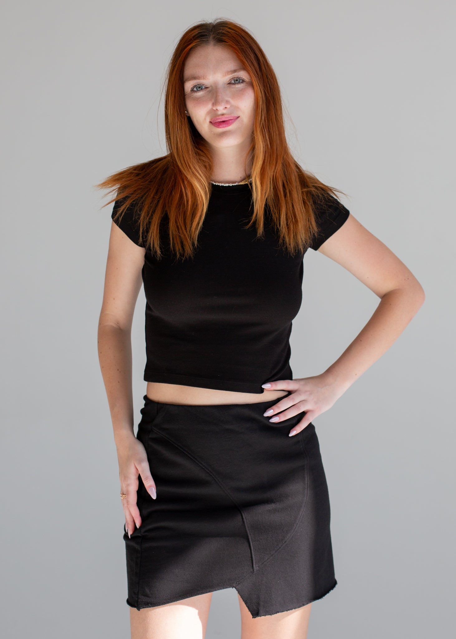 Woman wearing a black top and skirt against a gray background