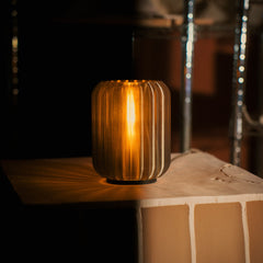 Decorative cylindrical lamp with ribbed design on a wooden surface