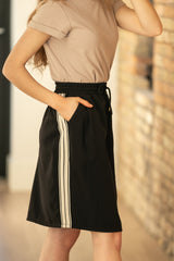 Person wearing a beige top and black skirt with white stripes outdoors.
