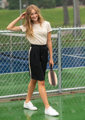 Woman on a tennis court holding a paddle, wearing a white shirt and black shorts with a white stripe.