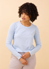 Woman wearing a light blue long-sleeve top against a beige background