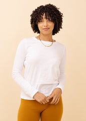 Woman wearing a white long-sleeve shirt and mustard pants against a beige background