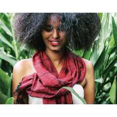 Woman wearing a red scarf in a natural setting with green foliage.
