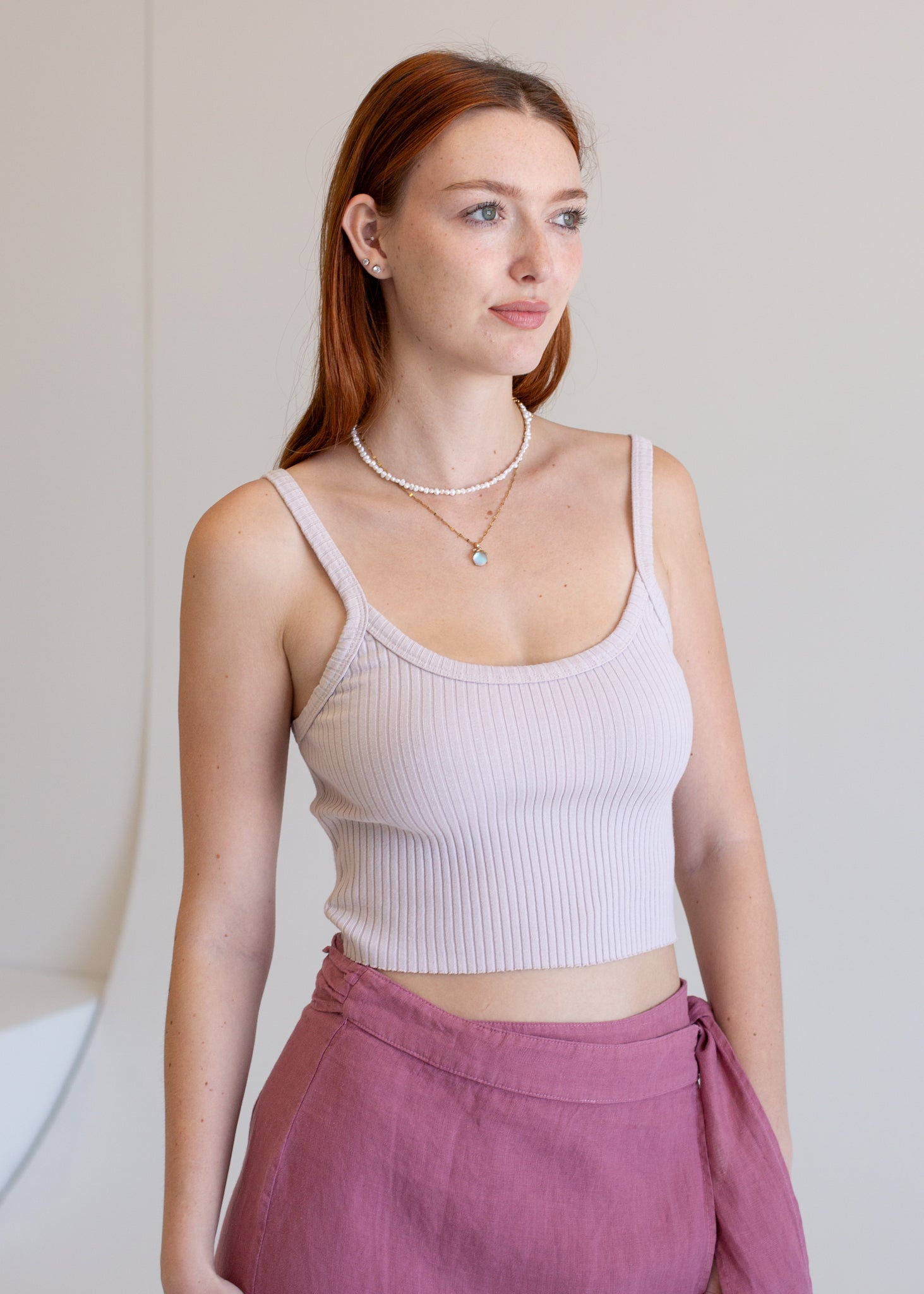 Woman wearing a light pink ribbed tank top and pink pants against a plain background