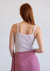 Woman wearing a white ribbed tank top and pink skirt against a plain background