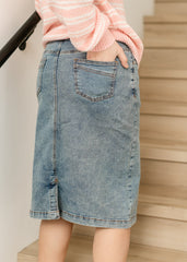Person wearing a pink sweater and denim skirt standing on a staircase.