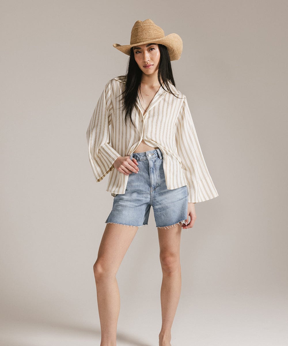 Woman wearing a striped shirt, denim shorts, and a straw hat on a plain background