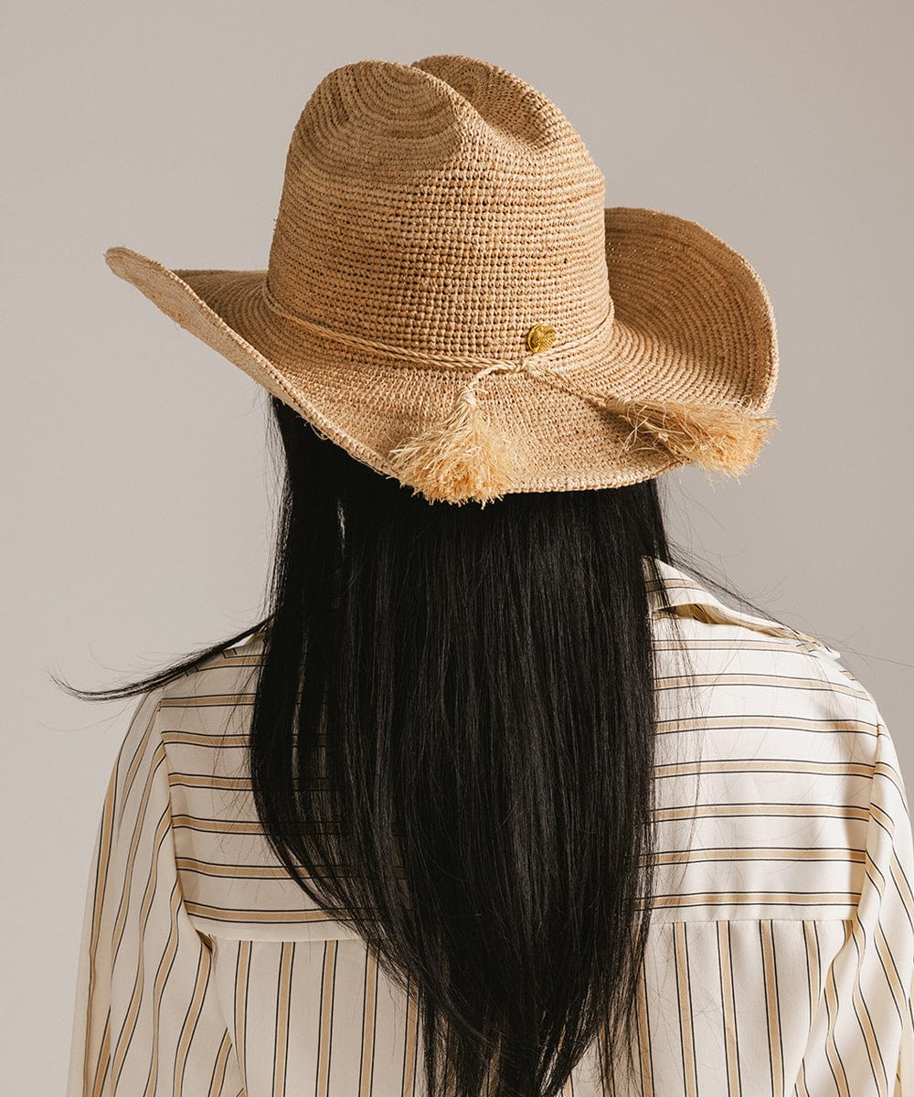 Person wearing a straw hat with a feather on a plain background