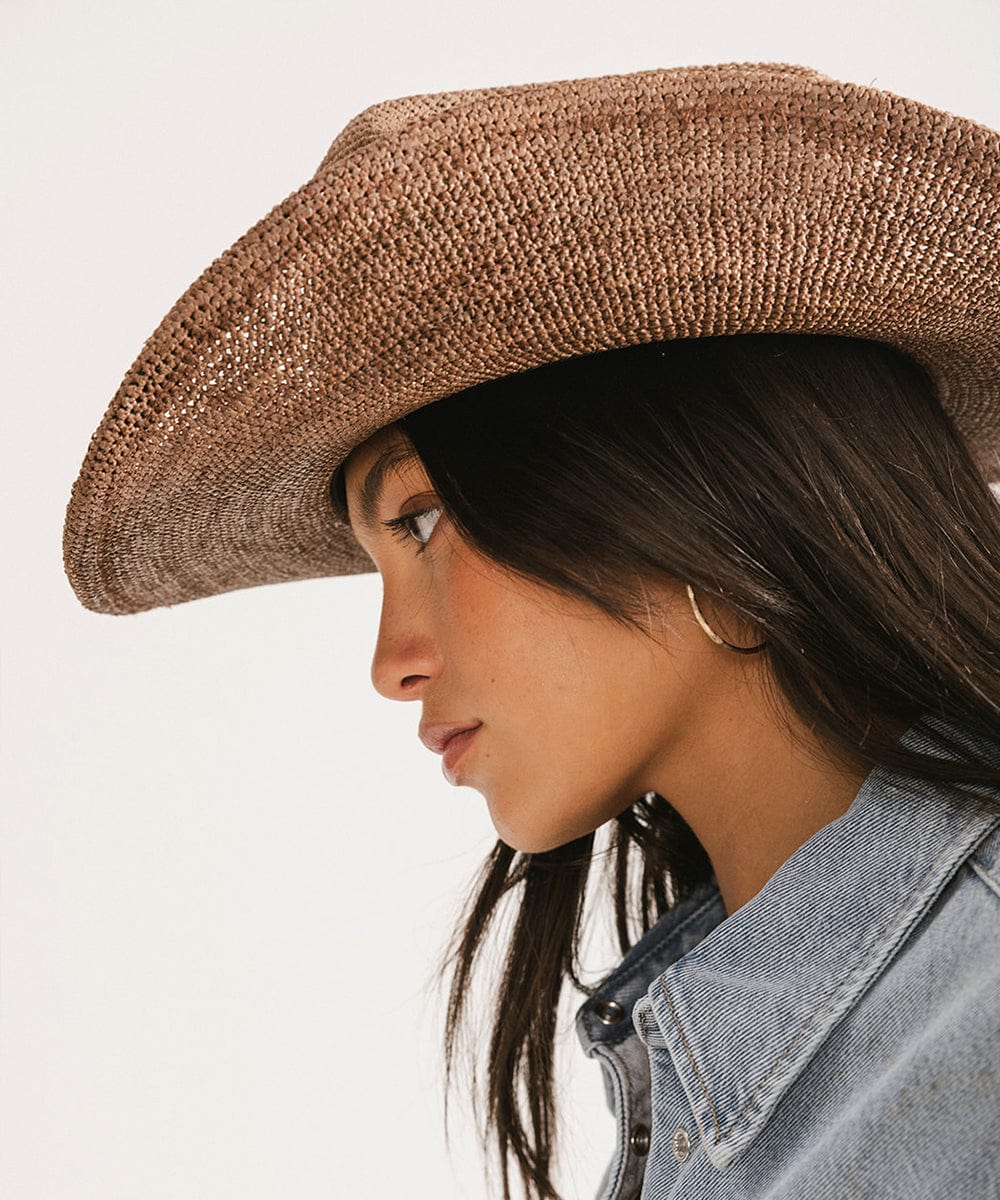 Woman wearing a brown cowboy hat and denim jacket on a light background