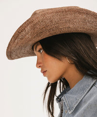 Woman wearing a brown cowboy hat and denim jacket on a light background