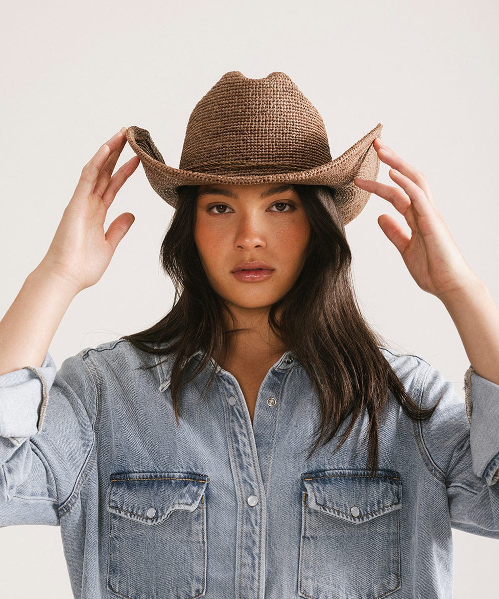 Woman wearing a straw cowboy hat and denim shirt against a plain background