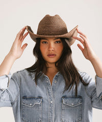 Woman wearing a straw cowboy hat and denim shirt against a plain background