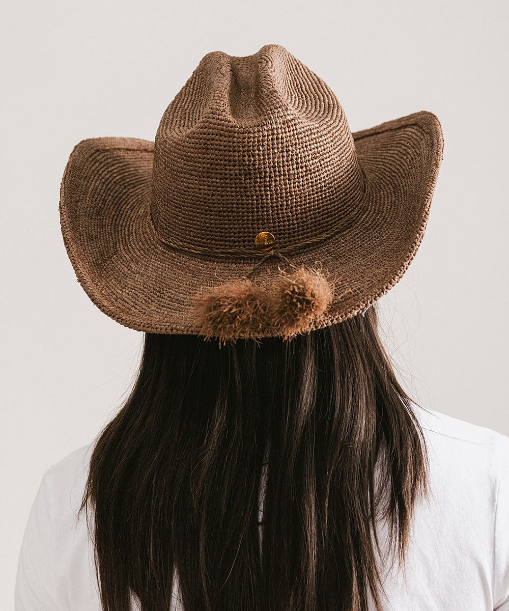 Brown cowboy hat with pom-poms on a plain background