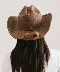 Brown cowboy hat with pom-poms on a plain background